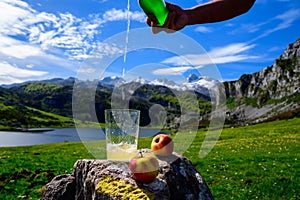 Pouring of natural Asturian cider made fromÂ fermented apples from green bottle and high height with view on Covadonga lake and